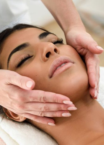 A person lying down with their eyes closed, receiving a facial massage from a professional, satified with her Build Your Package deal